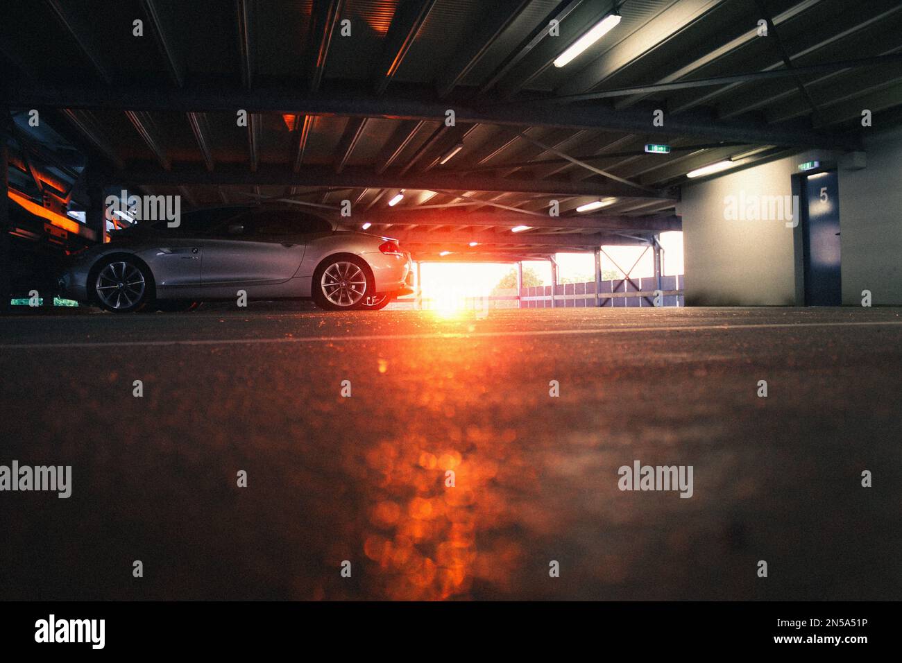 Uno scatto verticale di una BMW Z4 in un garage al tramonto. Il sole splende sull'auto in arancione. Foto Stock