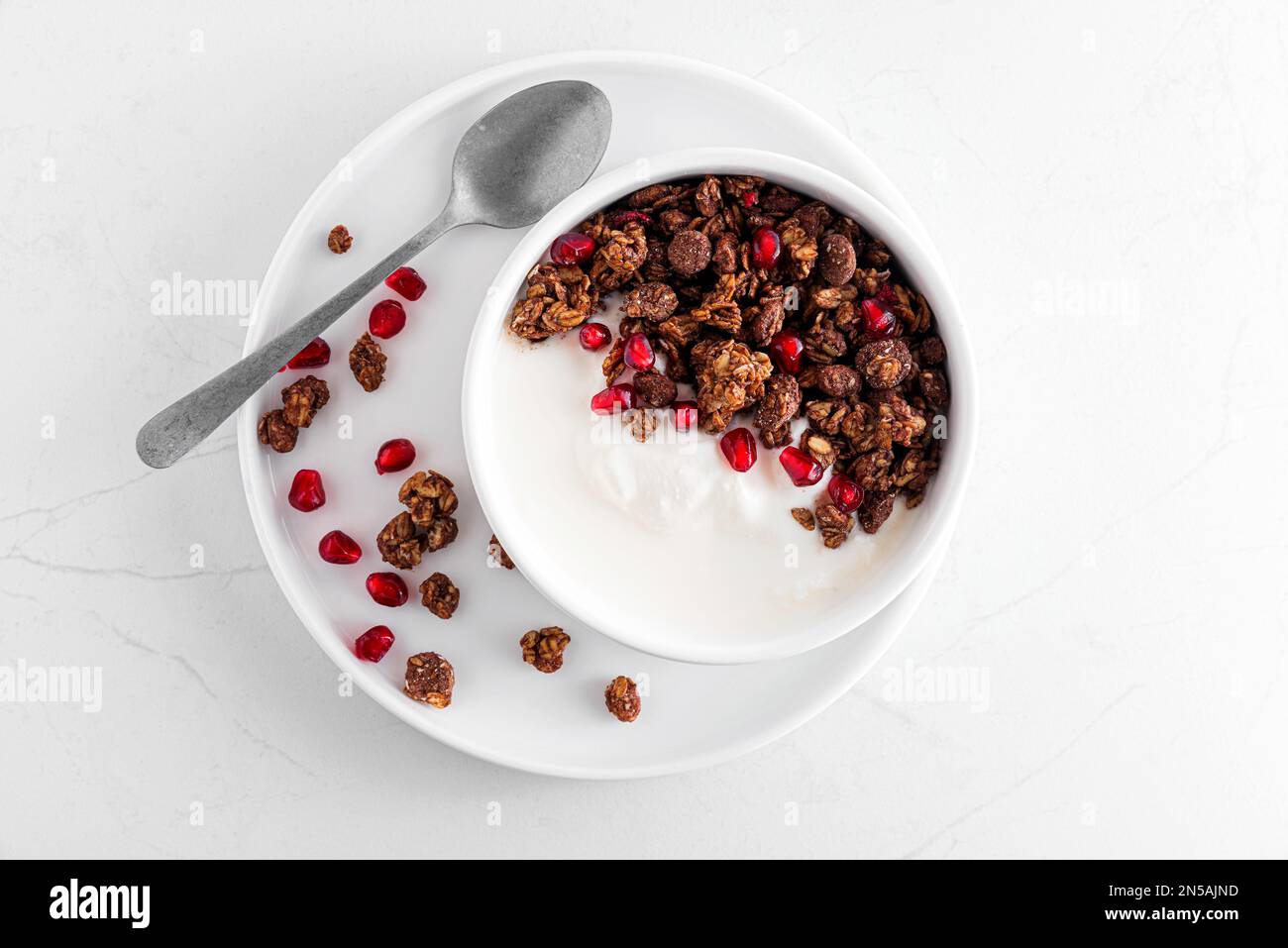 Colazione sana. Ciotola di yogurt greco con granola di avena al cioccolato e semi di melograno su tavola di marmo bianco. Vista dall'alto Foto Stock