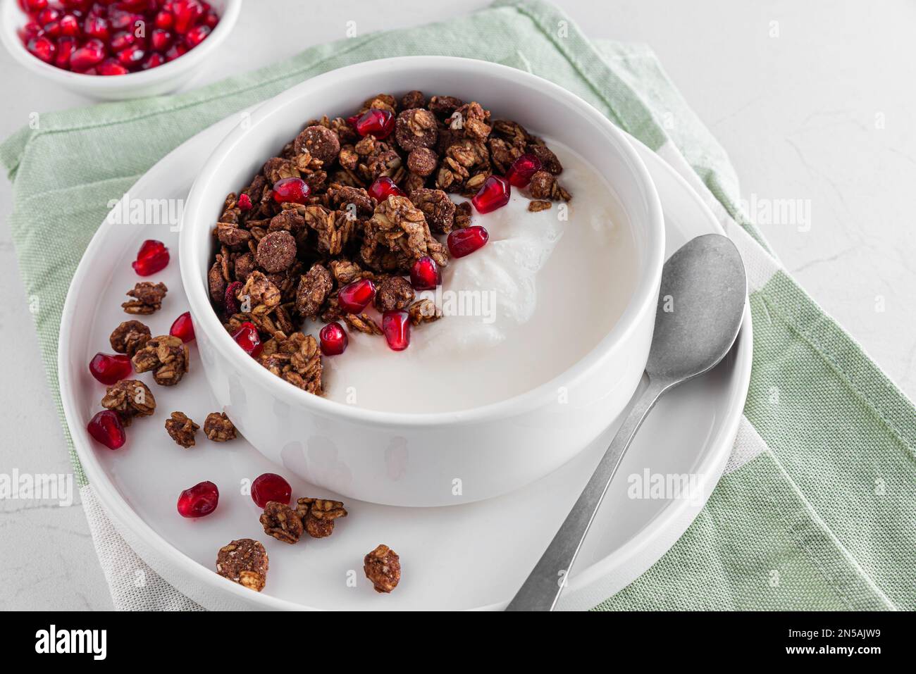 Ciotola di yogurt greco con granola di avena al cioccolato e semi di melograno su tavola di marmo bianco. Colazione sana Foto Stock