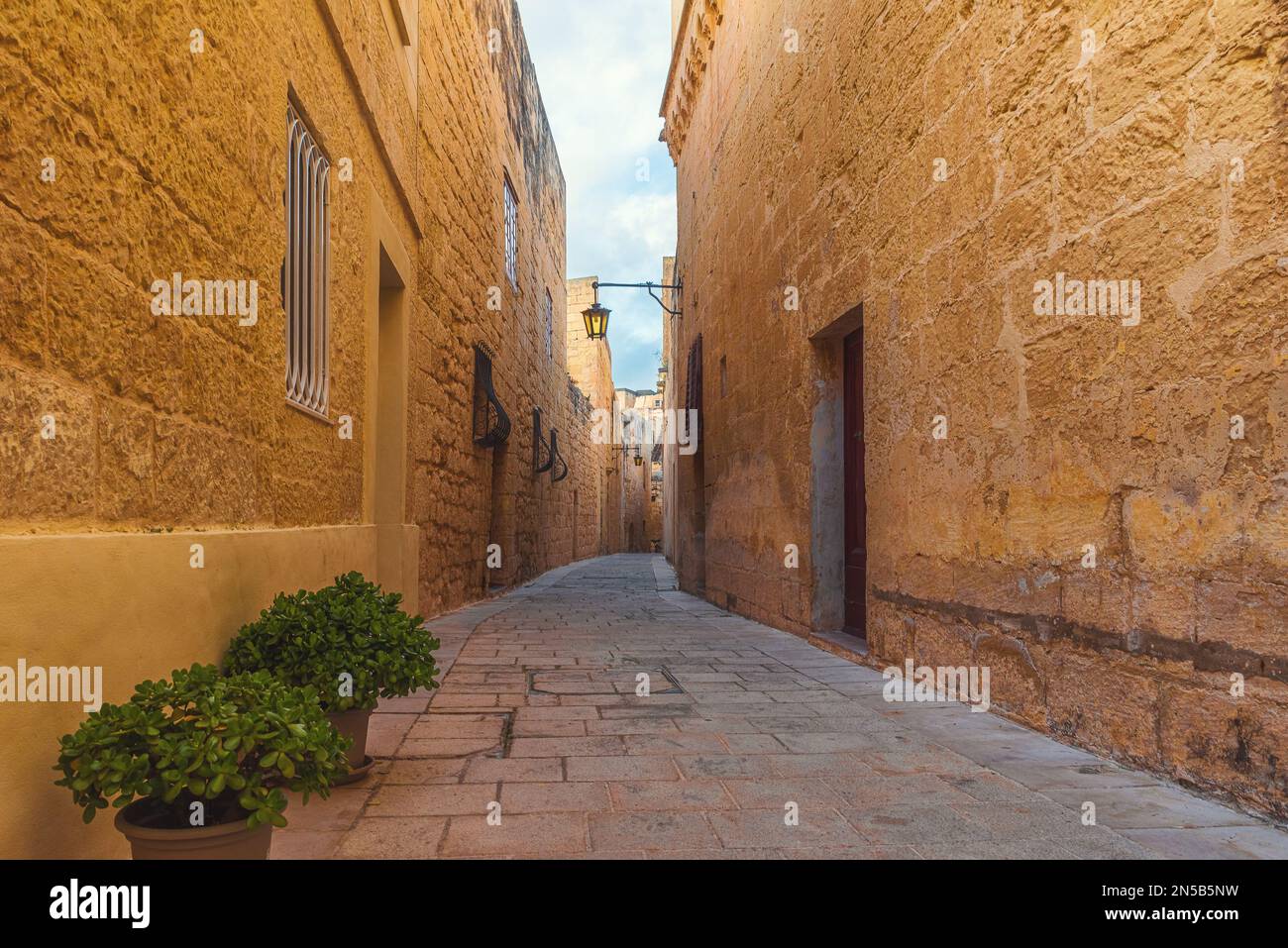 Vecchia strada medievale con luci di strada e vasi di fiori nella città di Mdina, Malta con nessuno. Destinazione di viaggio in Europa Foto Stock