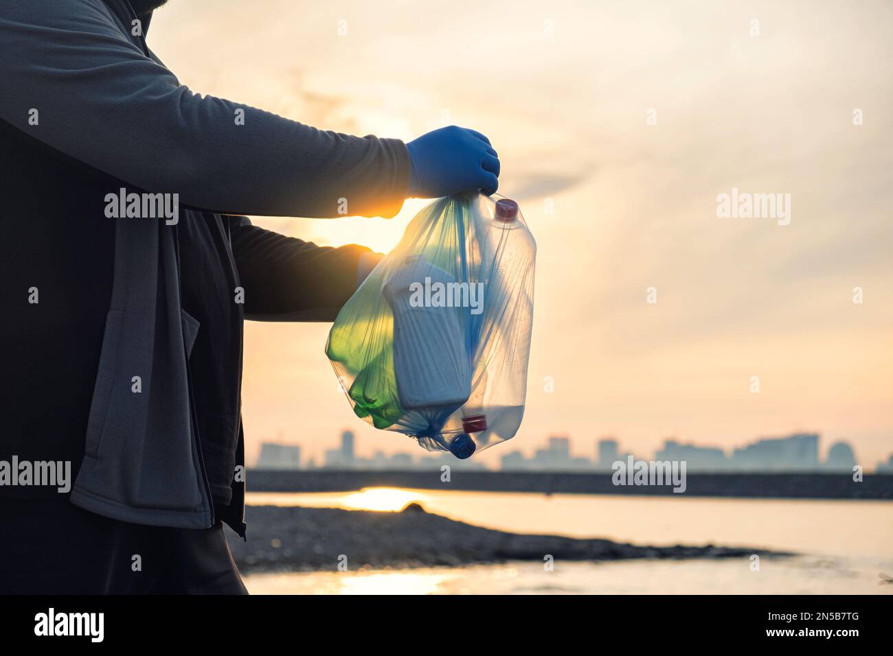 L'uomo tiene bottiglie di plastica in una borsa per rifiuti sulla spiaggia della città di Batumi. Concetto di inquinamento ambientale. Raccolta volontaria rifiuti riciclati Foto Stock