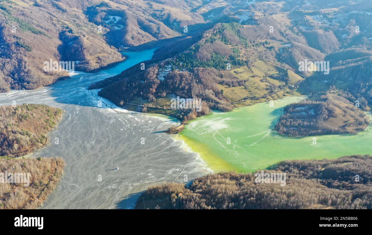 Veduta aerea del villaggio di Geamana affondata in un lago ghiacciato. Separazione chiara tra i residui di prospezione dei minerali e l'acqua limpida. Guglia della chiesa Foto Stock