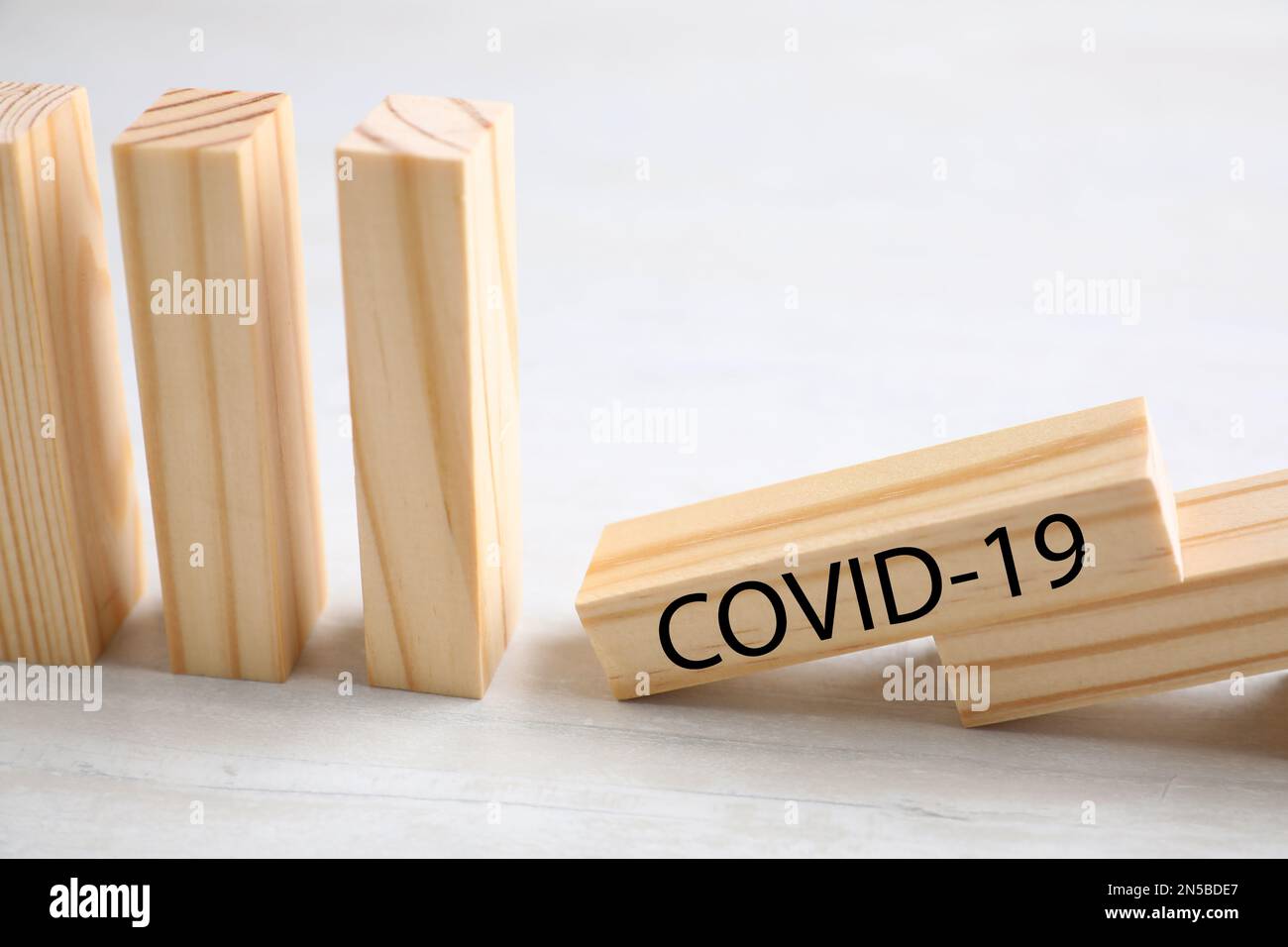 Piastrelle di legno domino su tavolo bianco, primo piano. Diffusione del concetto di coronavirus Foto Stock