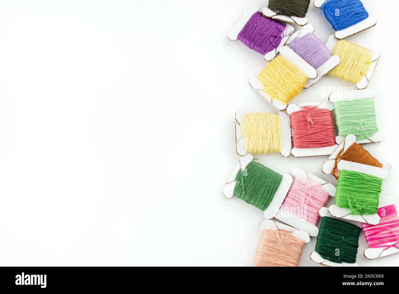 Matasse di fili di cotone di diversi colori giacciono sul lato destro della cornice su sfondo bianco Foto Stock