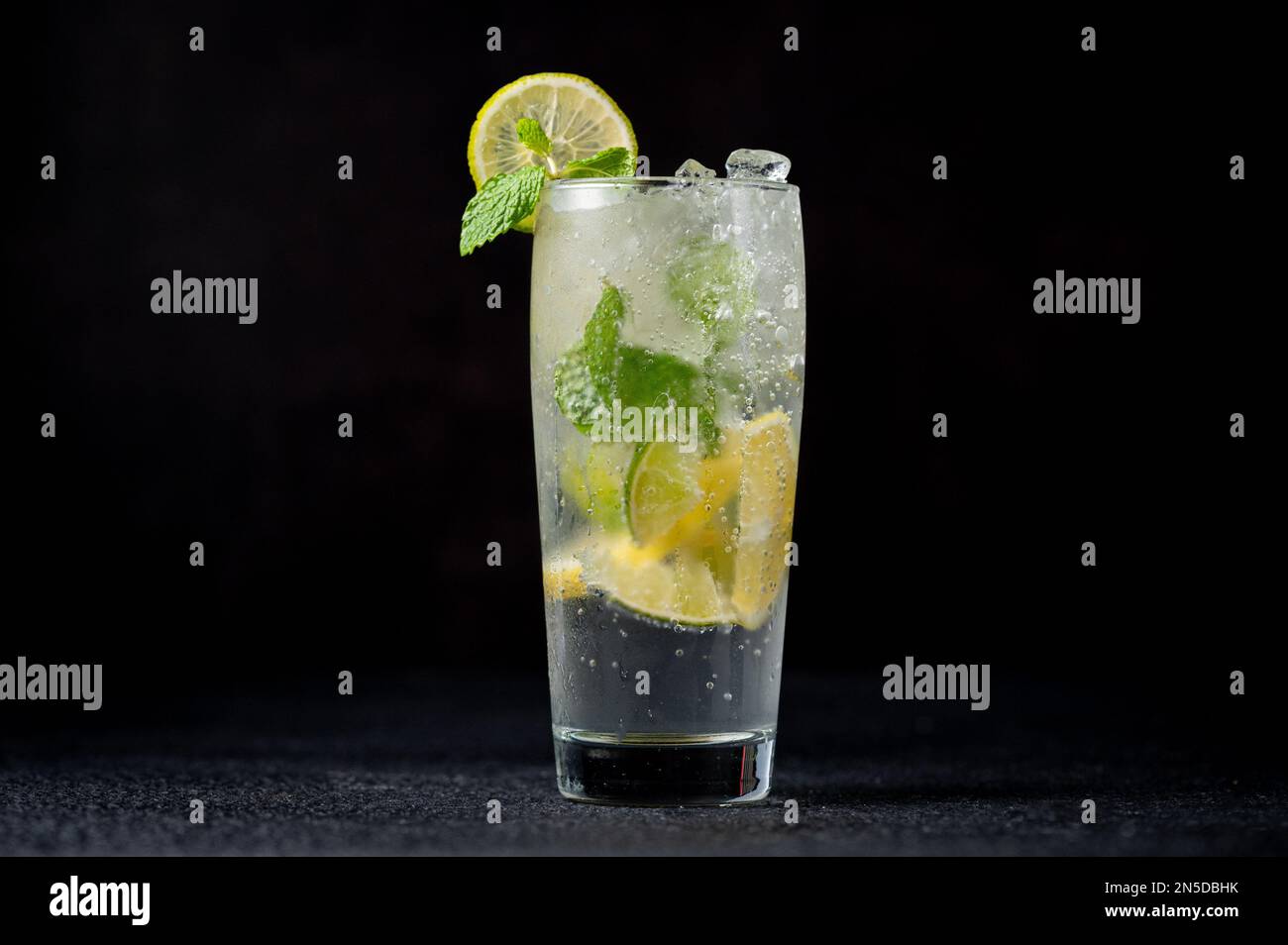 Un bicchiere alto riempito di Mojito rinfrescante con fette di lime Foto Stock