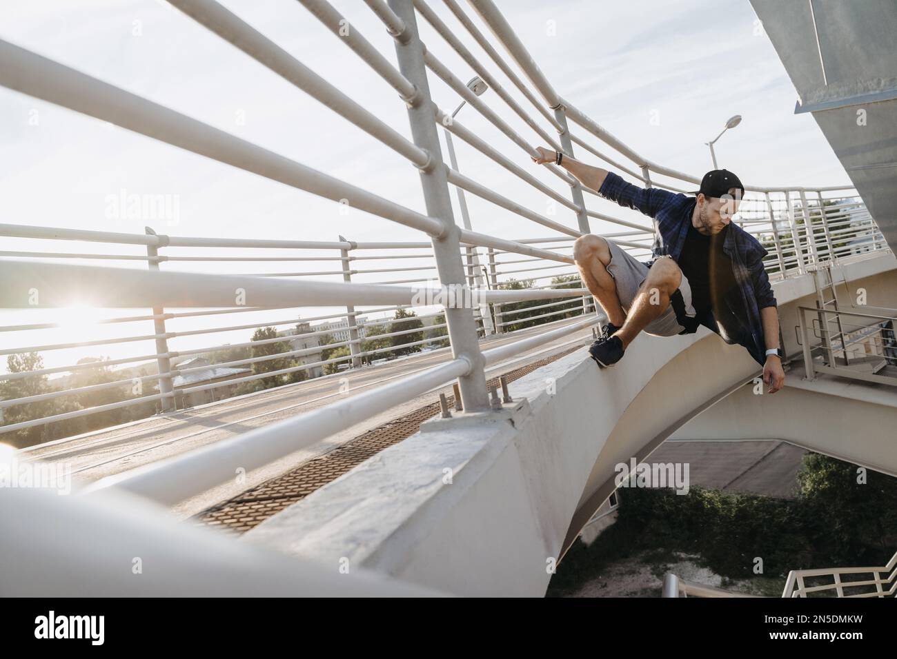 Parkour atleta appeso al ponte e pronto per il salto pericoloso. Freerunning in città Foto Stock