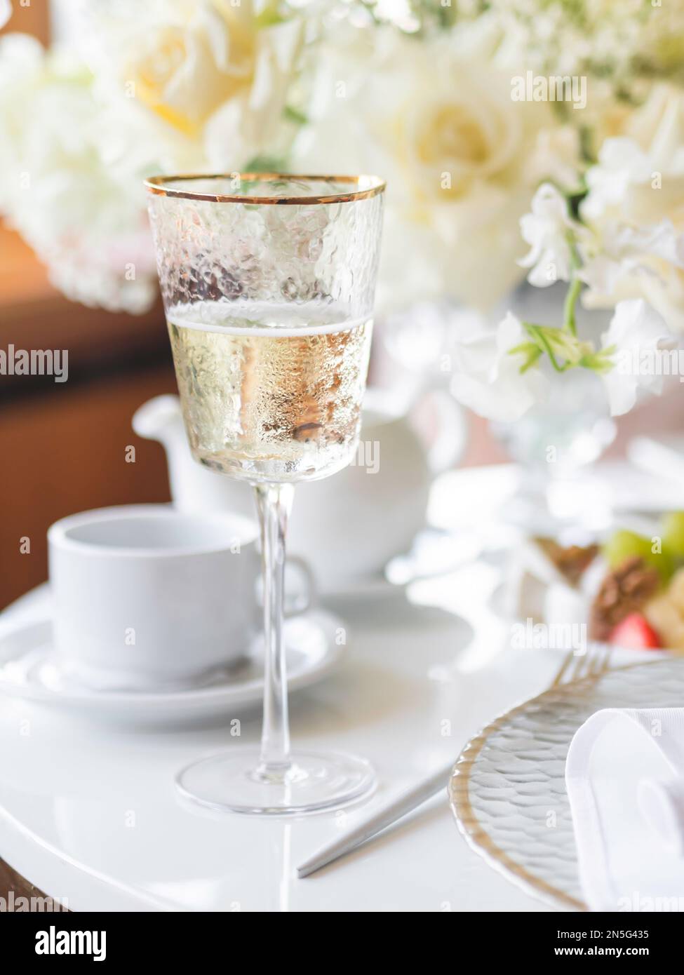 Il tavolo serve per banchetti. Champagne in un moderno bicchiere di vino, piatti con tovaglioli e posate lucenti su un panno da tavolo bianco. Foto Stock