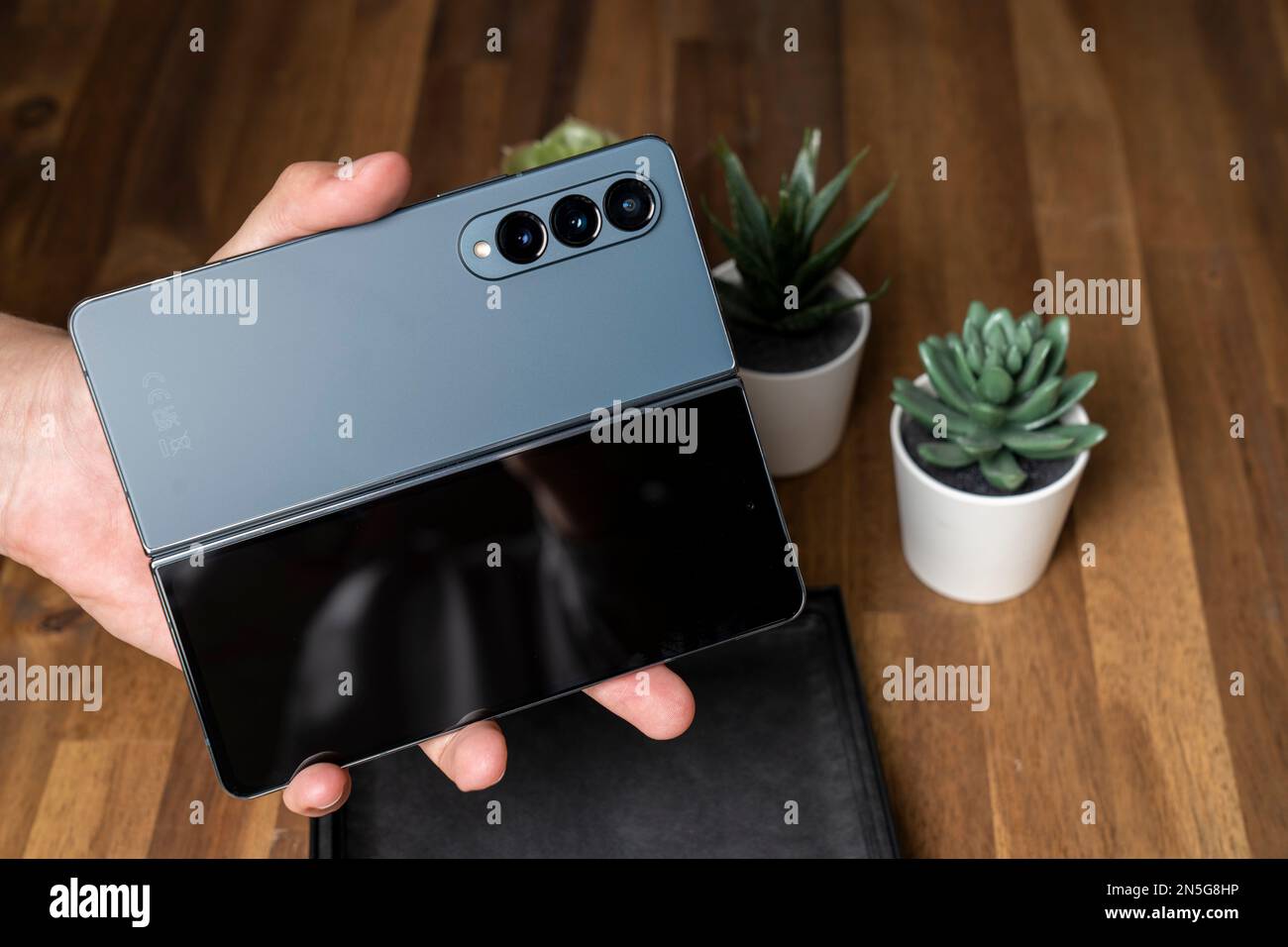 Samsung Galaxy Z Fold 4 in colore grigio-verde. Il dispositivo in posizione aperta nelle mani di un uomo. Un tavolo di legno nel Foto Stock