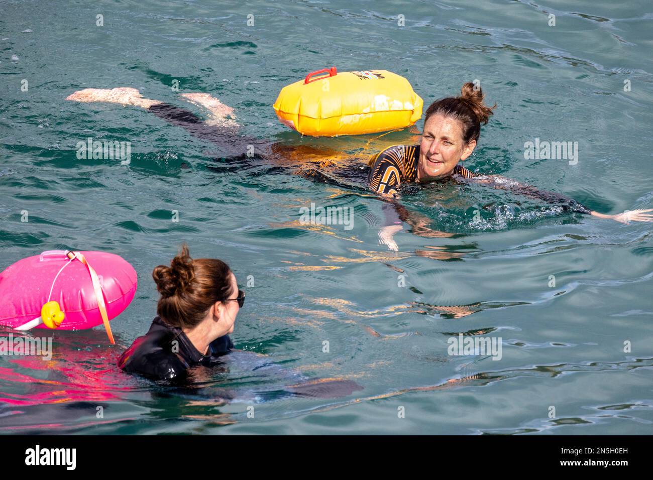 Nuotatori selvatici che nuotano attraverso la baia di Coveack in autunno. Segnano la loro posizione in acqua con un galleggiante ad alta visibilità Foto Stock