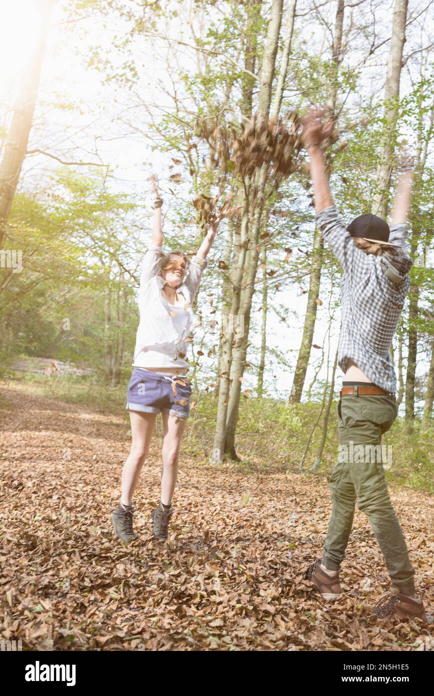 Giovane coppia che gioca con le foglie autunnali in una foresta, Baviera, Germania Foto Stock