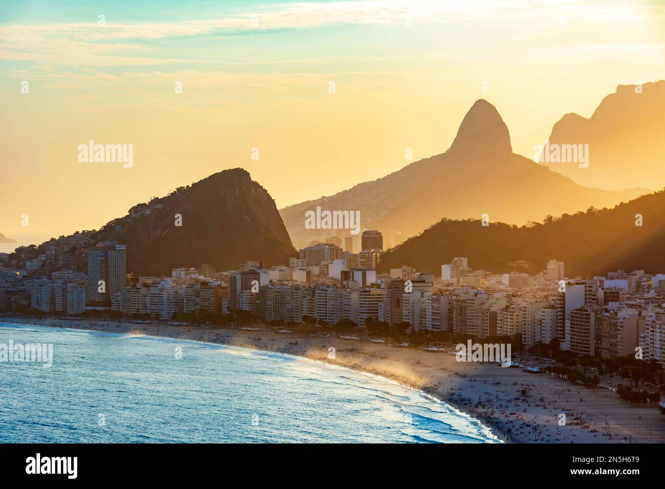 Tramonto sulla spiaggia di Copacabana a Rio de Janeiro con la luce proveniente da dietro gli edifici e le colline Foto Stock