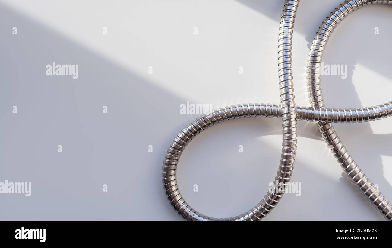 Tubo doccia in metallo su sfondo bianco. Tubo cromato flessibile. Tubo corrugato su striscione geometrico con spazio copia su luce solare dura Foto Stock