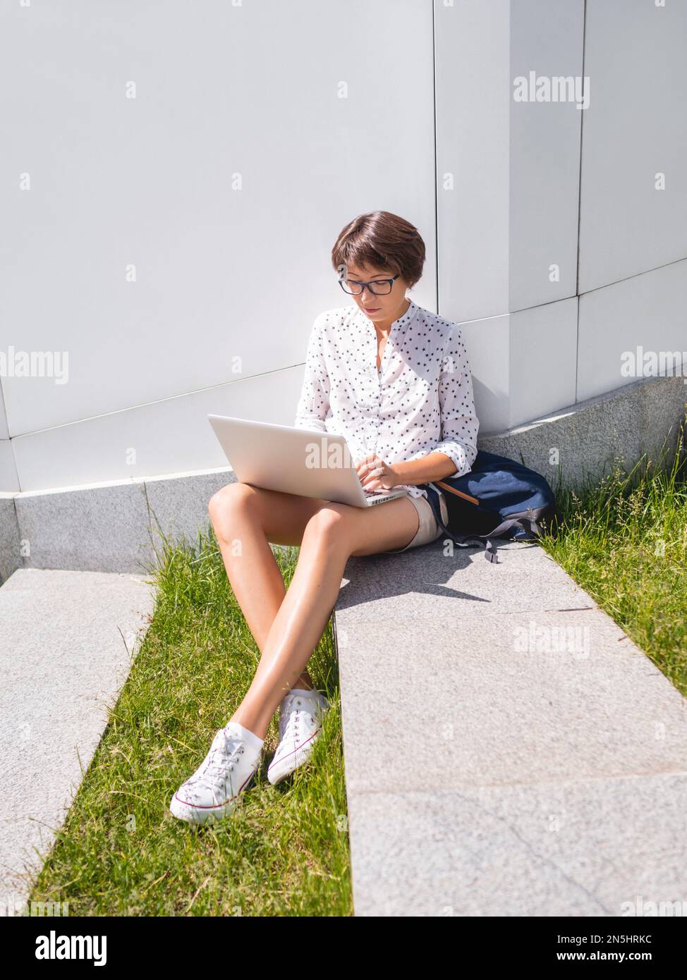 Donna seduto con un notebook sulla panca del parco urbano. Freelance al lavoro. Gli studenti imparano a distanza dall'esterno. Stile di vita moderno. Atmosfera estiva. Foto Stock