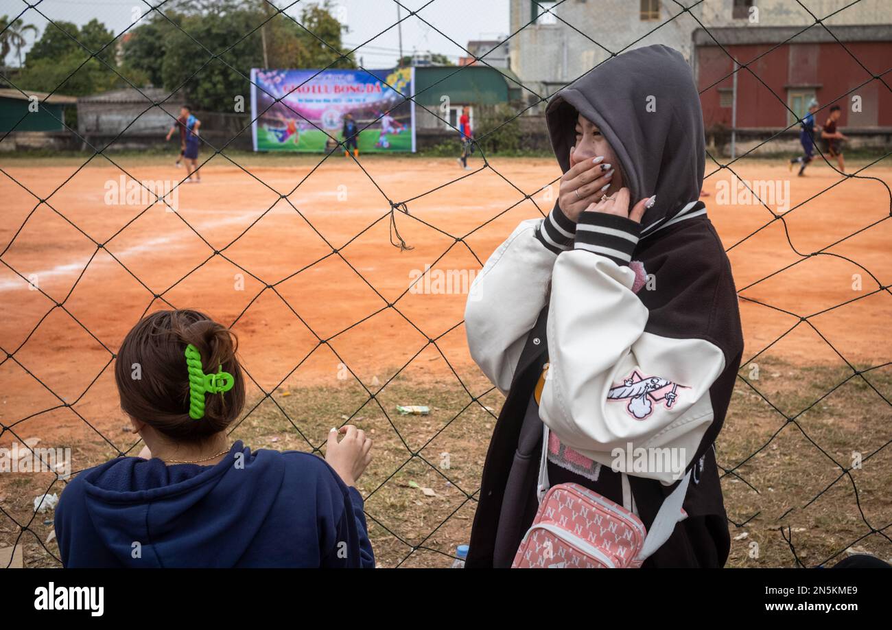 Una ragazza si nasconde il viso mentre ride con la sua amica dopo essere venuta a guardare una partita di calcio locale a tra Co, vicino Mong Cai a Quang Ninh, Vietnam Foto Stock