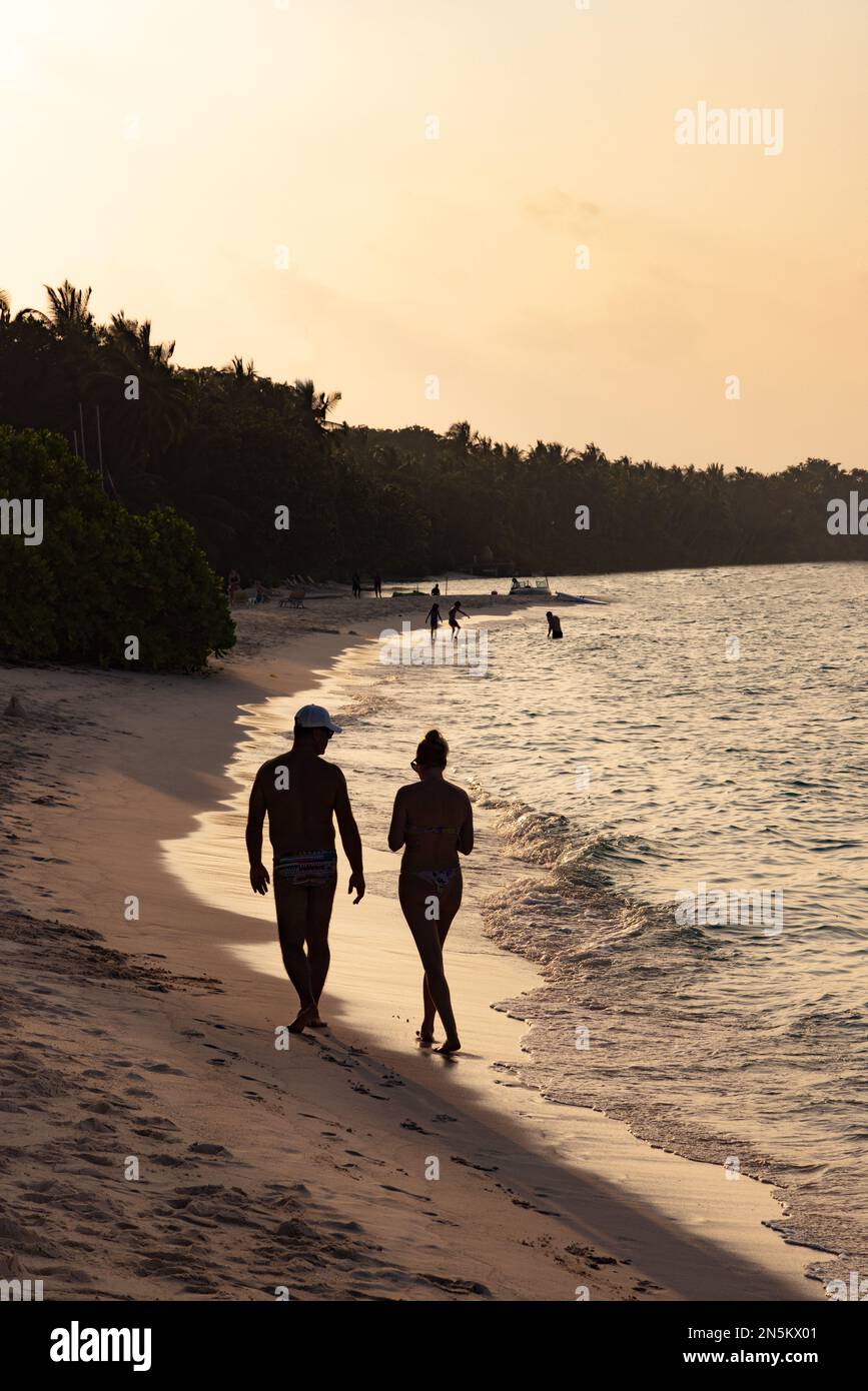 Maldive spiaggia - una coppia in una vacanza a lungo raggio a piedi al bordo delle acque su una spiaggia di sabbia al tramonto, Rasdhoo Atoll, le Maldive, Oceano Indiano Asia Foto Stock