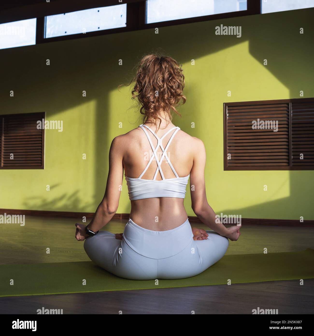 Giovane donna atletica che pratica yoga medita mentre si siede in una posizione di loto, esercitandosi in sportswear bianco in un'esercitazione di idoneità, seduta con lei Foto Stock