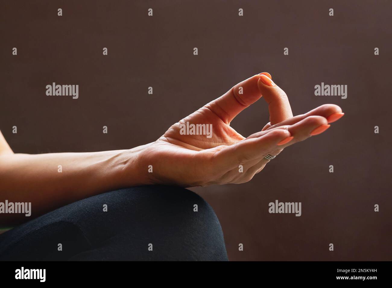 Una donna che pratica yoga, mostra il simbolo di jnana mudra o mudra della conoscenza su uno sfondo scuro, primo piano Foto Stock