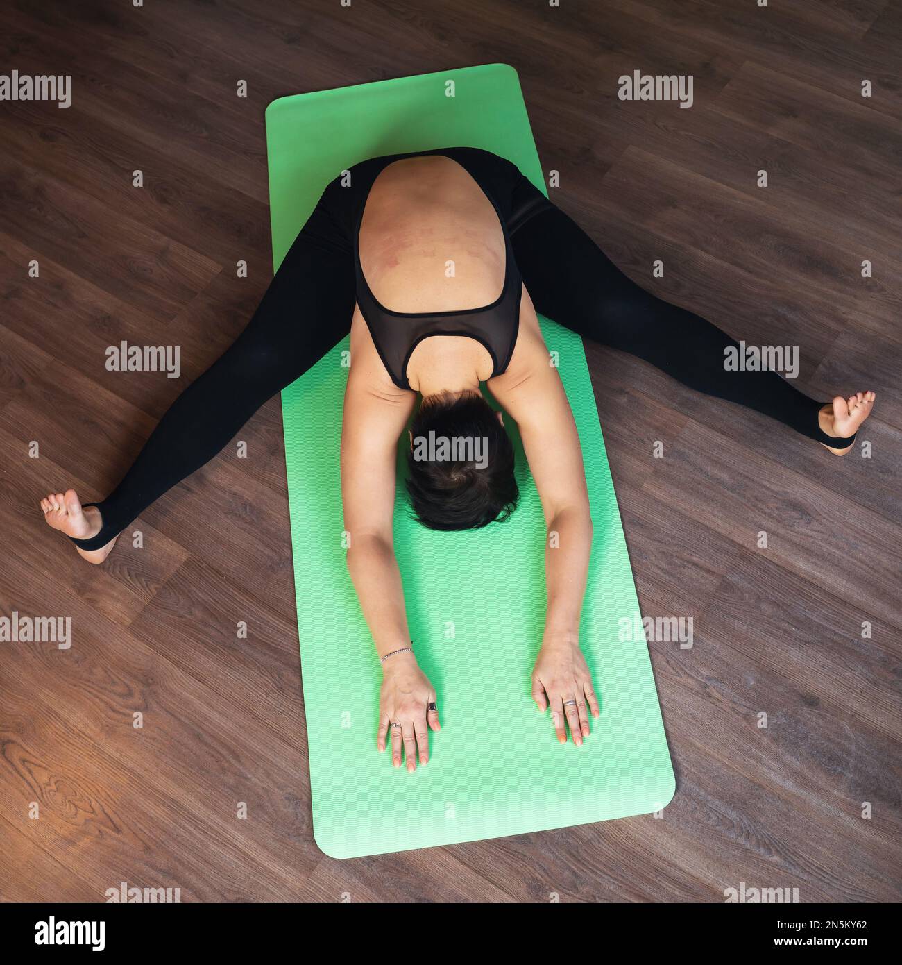 Una donna di mezza età conduce uno stile di vita sano e pratica yoga, esegue l'esercizio Samakonasana, spaccatura trasversale con una curva in avanti, allena alo Foto Stock