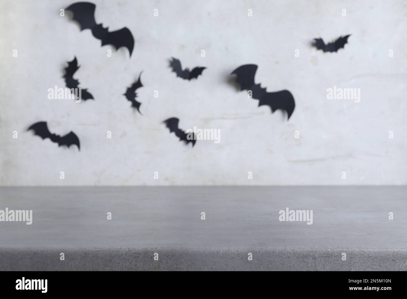 Tavolo di pietra vicino al muro grigio con pipistrelli di carta nera. Decorazione di Halloween Foto Stock