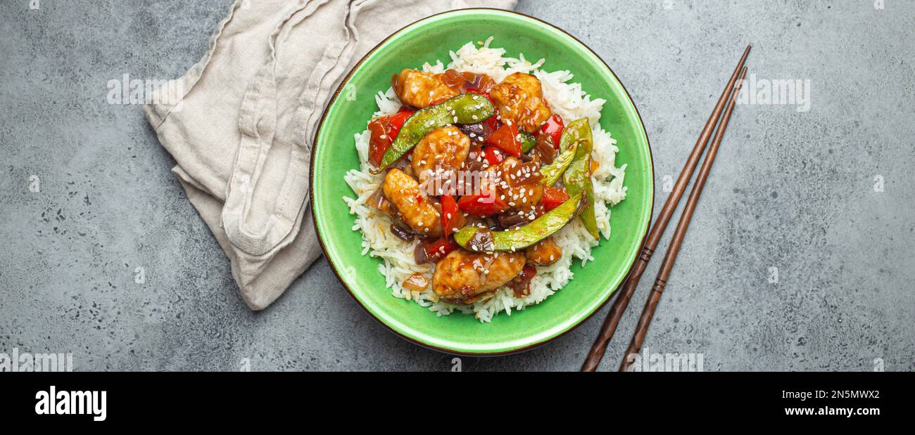 Pollo asiatico dolce e acaro appiccicoso con verdure saltate e riso in ciotola di ceramica con vista dall'alto chopsticks, sfondo grigio pietra rustica Foto Stock