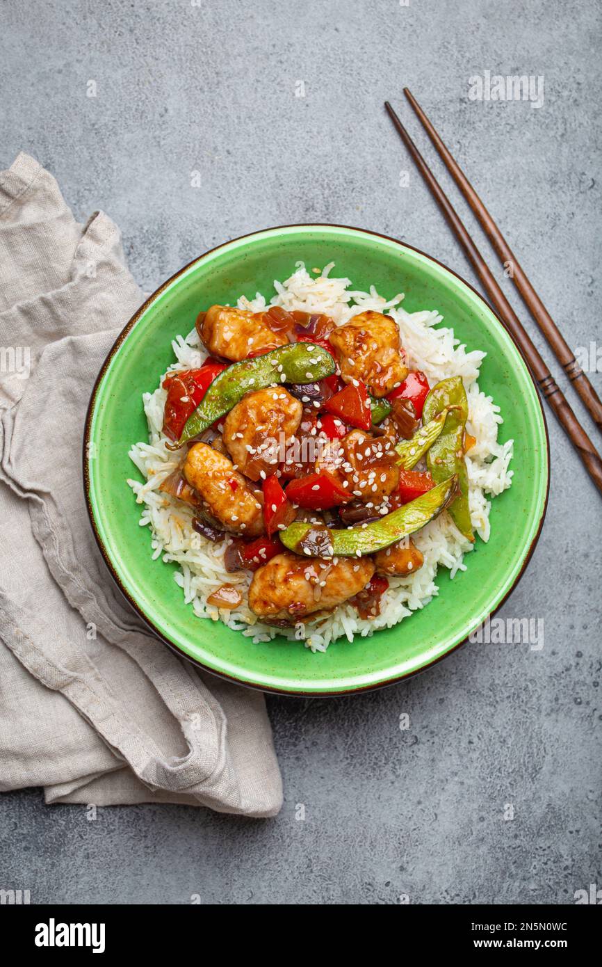 Pollo asiatico dolce e acaro appiccicoso con verdure saltate e riso in ciotola di ceramica con vista dall'alto chopsticks, sfondo grigio pietra rustica Foto Stock