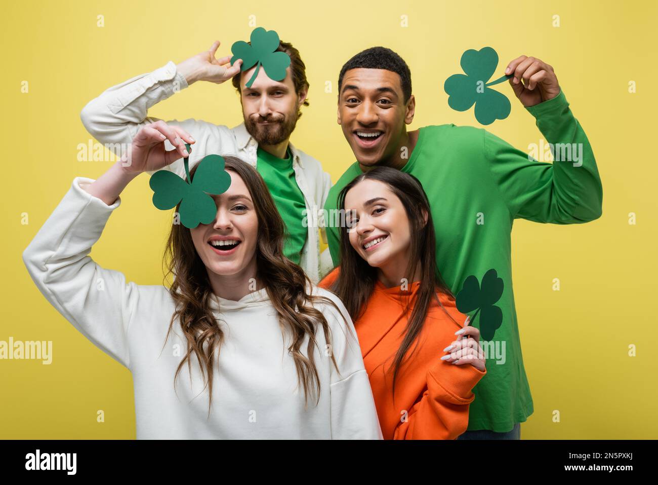 Amici multietnici sorridenti che si divertono con il trifoglio di carta isolato sul giallo Foto Stock
