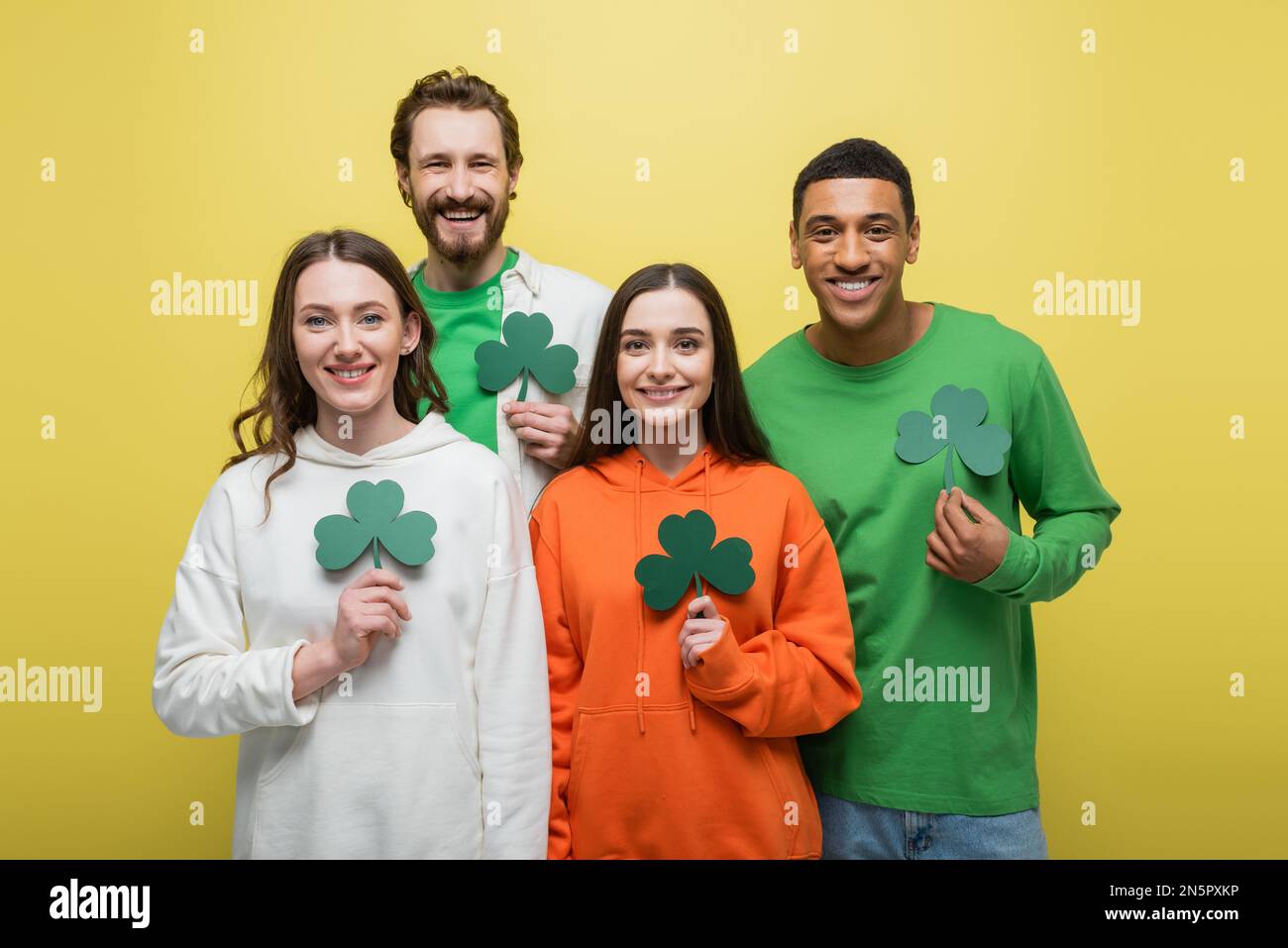Felice gente multietnica che tiene il trifoglio di carta isolato su giallo Foto Stock