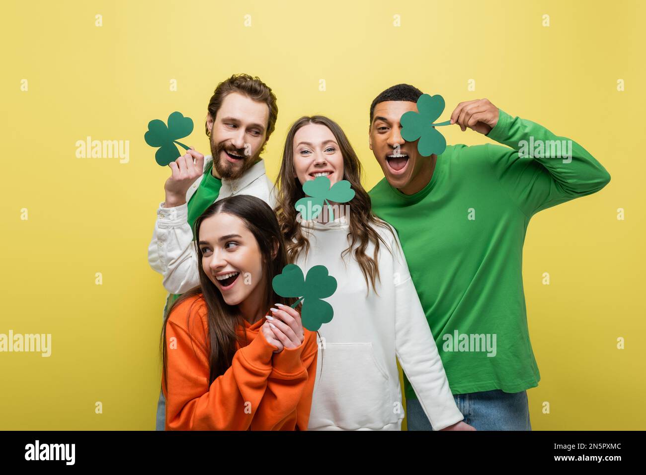 Allegri amici interracial che tengono il trifoglio di carta isolato su giallo Foto Stock