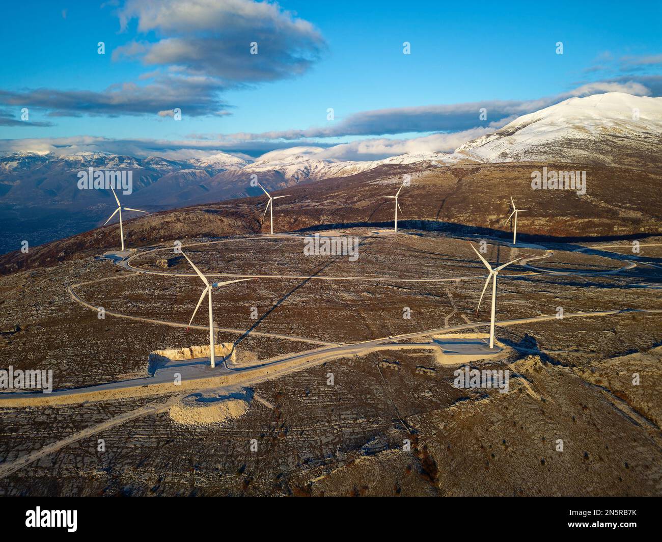 Mulini a vento sulle colline durante il tramonto. Energie rinnovabili, energia verde. Montagne sullo sfondo con la neve. Energia eolica e rispettosa dell'ambiente. Foto Stock