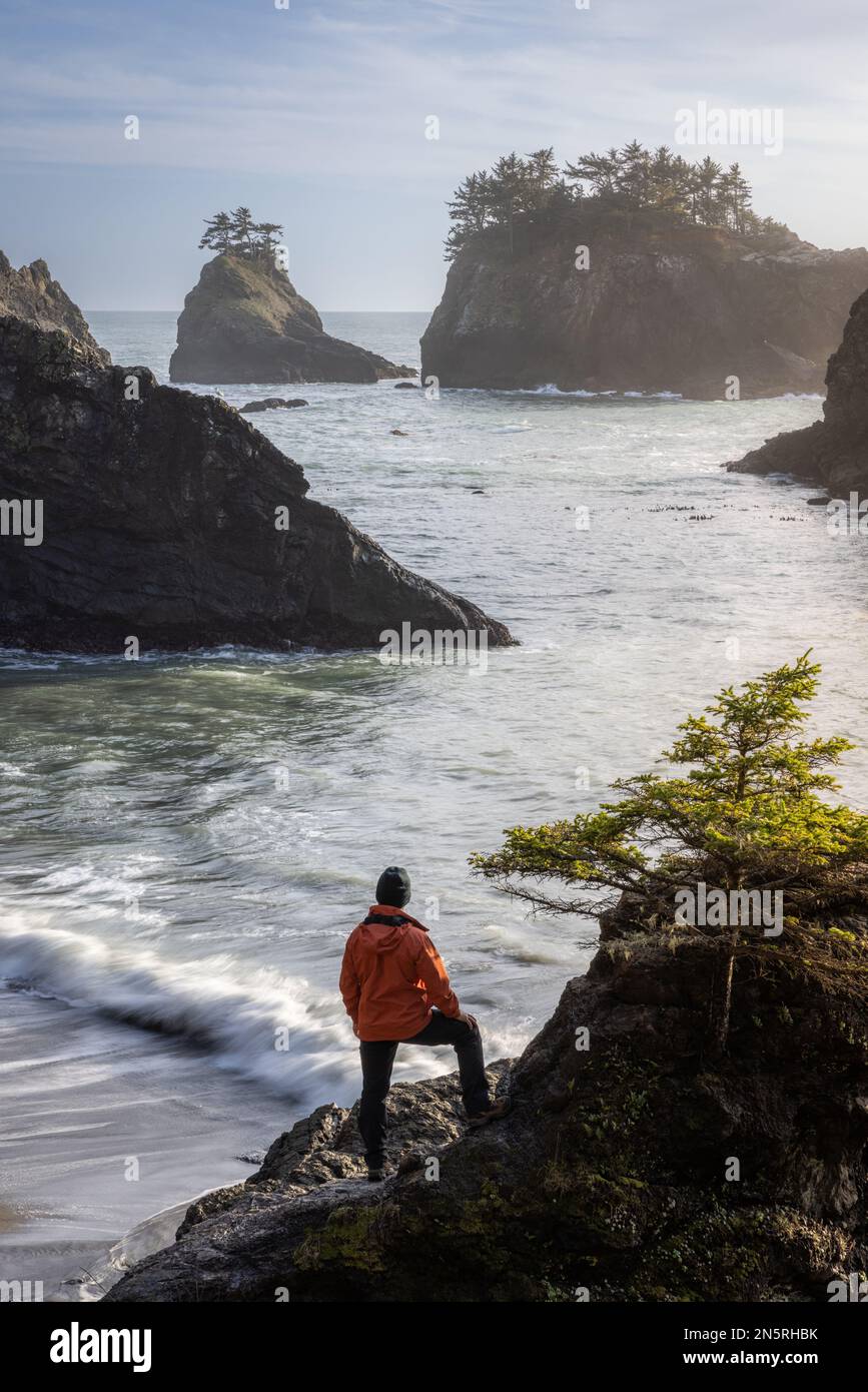 Uomo seduto su una roccia godendo della splendida vista del mare e delle pile di mare in questo bellissimo posto sulla costa dell'Oregon Foto Stock