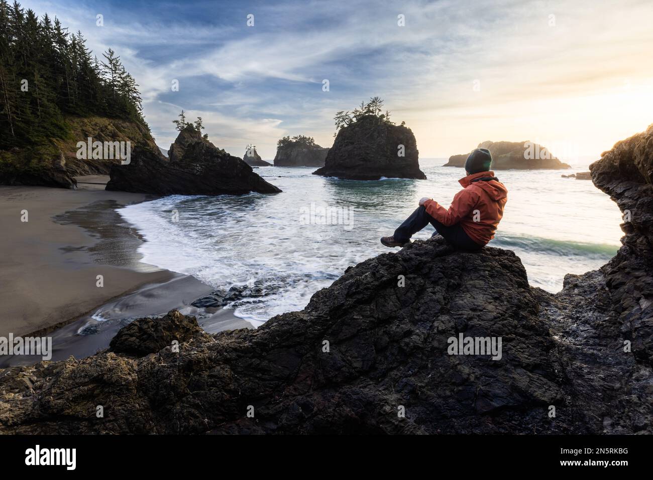 Uomo seduto su una roccia godendo della splendida vista del mare e delle pile di mare in questo bellissimo posto sulla costa dell'Oregon Foto Stock