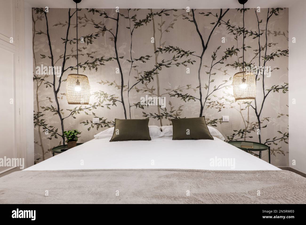 Camera da letto con letto matrimoniale senza testiera su una parete  tappezzata con bellissimi disegni di rami, cuscini verdi e comodini  circolari in metallo Foto stock - Alamy