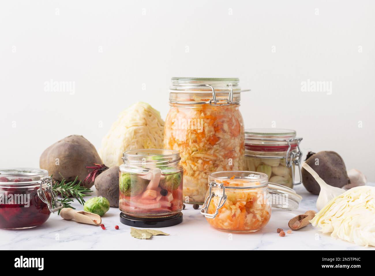 Vasetti di vetro con verdure e ingredienti vari in salamoia su sfondo marmoreo Foto Stock