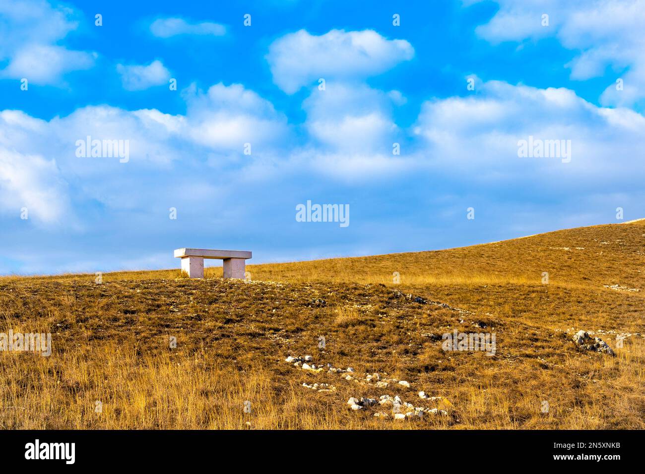 Panca in pietra bianca su una collina marrone con cielo blu Foto Stock