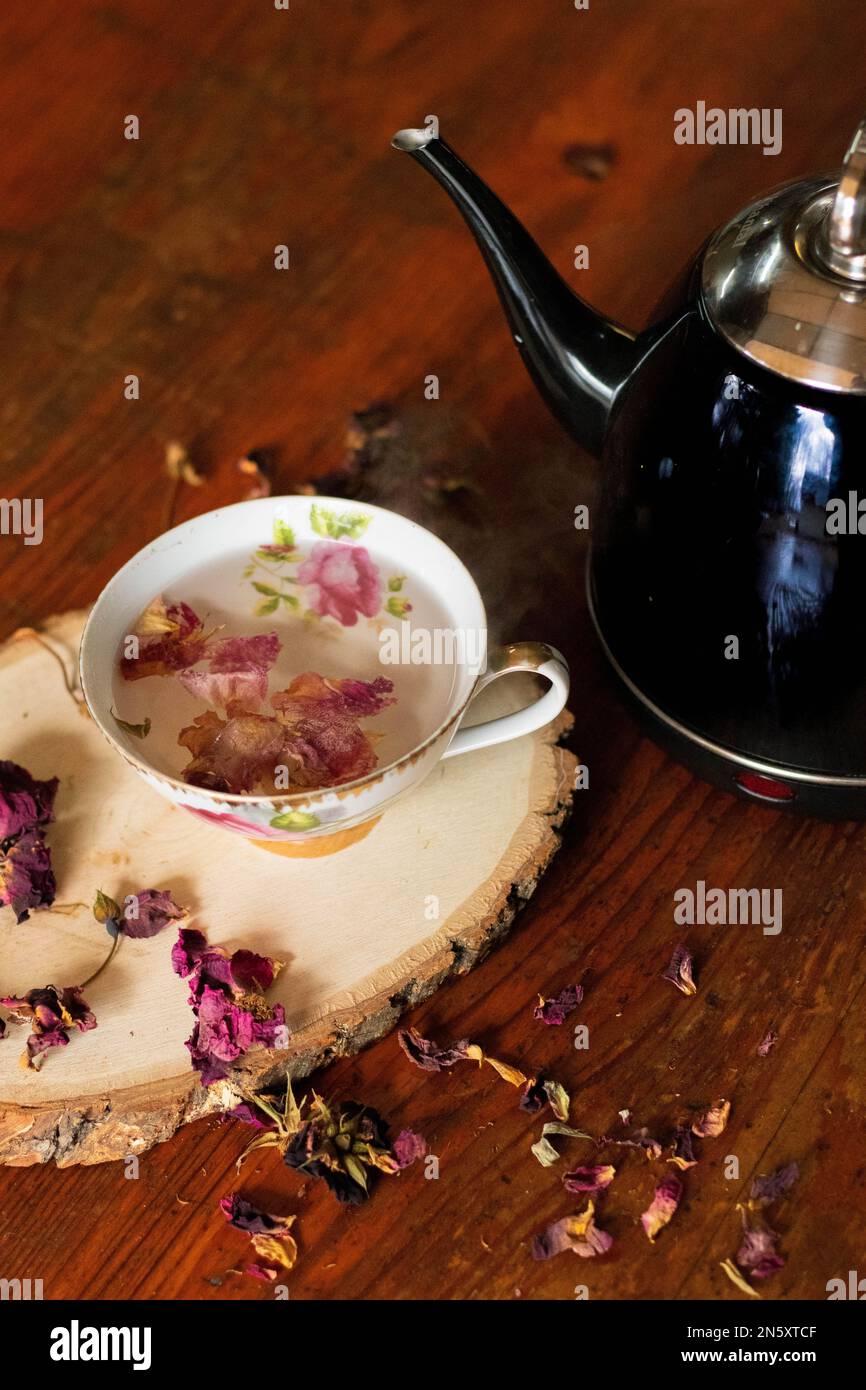 bollitore da tè nero accanto alla tazza da tè con fiori rosa Foto Stock