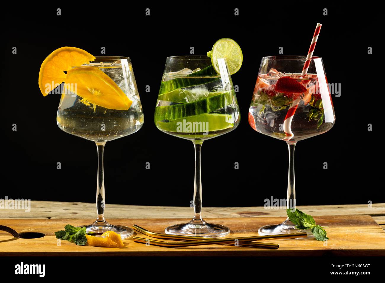 Tre bicchieri con acqua e frutta su tavola di legno su sfondo nero Foto Stock