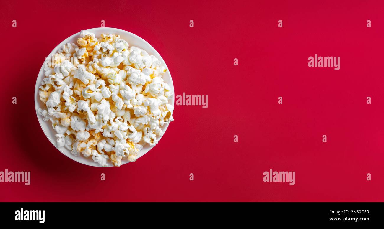 Formaggio saporito popcorn sparso in ciotola isolato su sfondo rosso. Sfondo, banner, intestazione con spazio di copia per il testo. Fast food, film, cinema ed e Foto Stock