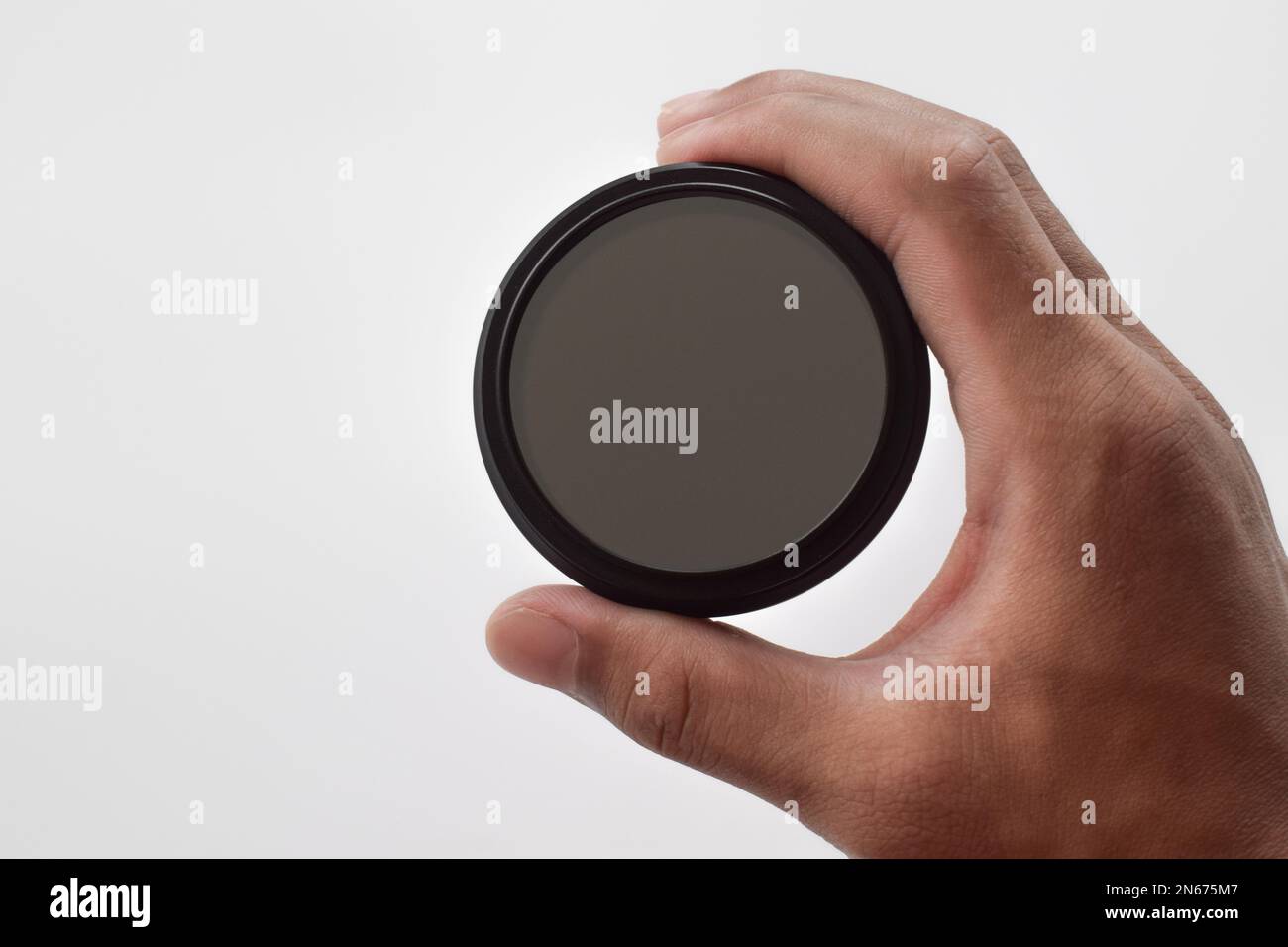 La mano dell'uomo tiene un filtro ottico ND (a densità neutra) isolato su sfondo bianco Foto Stock