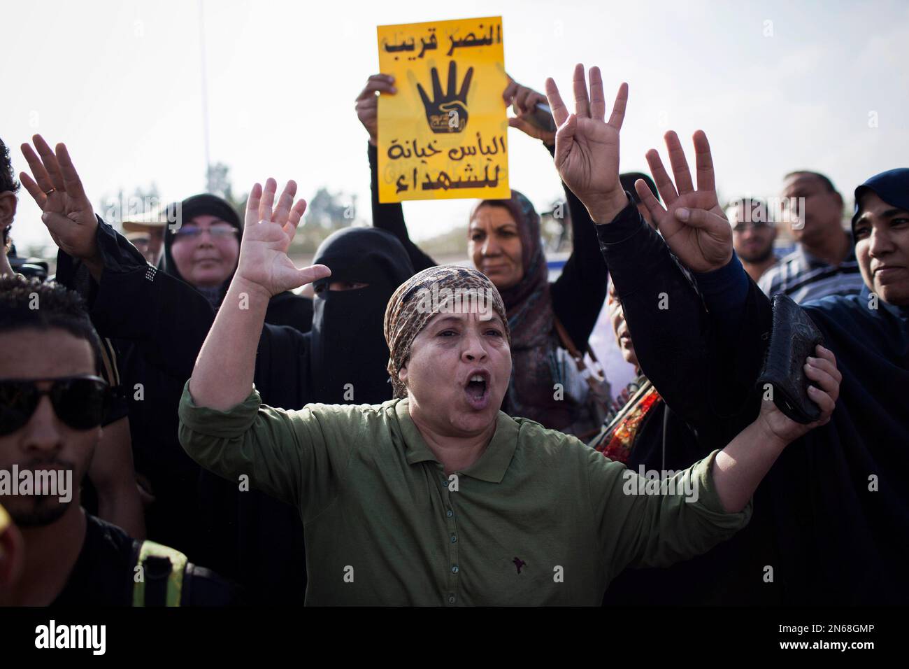 A supporter of Egypt's ousted President Mohammed Morsi chants slogans against the Egyptian Army outside of a police academy compound were the trial of ousted President Mohammed Morsi is held in Cairo, Egypt, Monday, Nov. 4 2013. Behind her, a woman holds a placard with Arabic that reads, "victory is coming, lost hope is betrayal to the marytrs," and four raised fingers, which has become a symbol of the Rabaah al-Adawiya mosque, where Morsi supporters had held a sit-in for weeks that was violently dispersed in August. Egypt's deposed Islamist president was brought from the secret location of hi Foto Stock