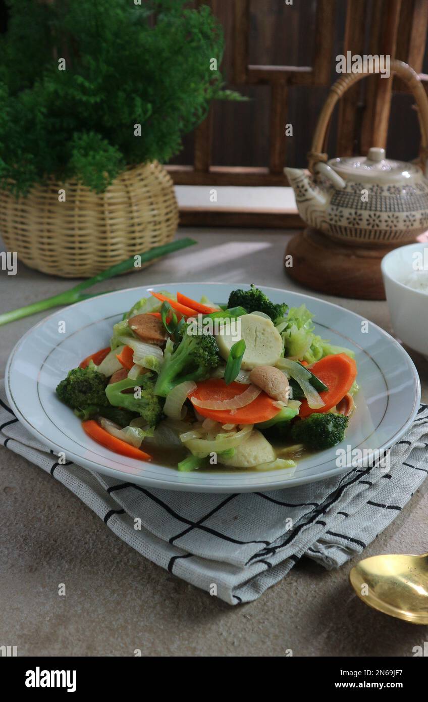 servizio di verdure fritte in padella su un piatto bianco primo piano con piante e teiere sullo sfondo Foto Stock