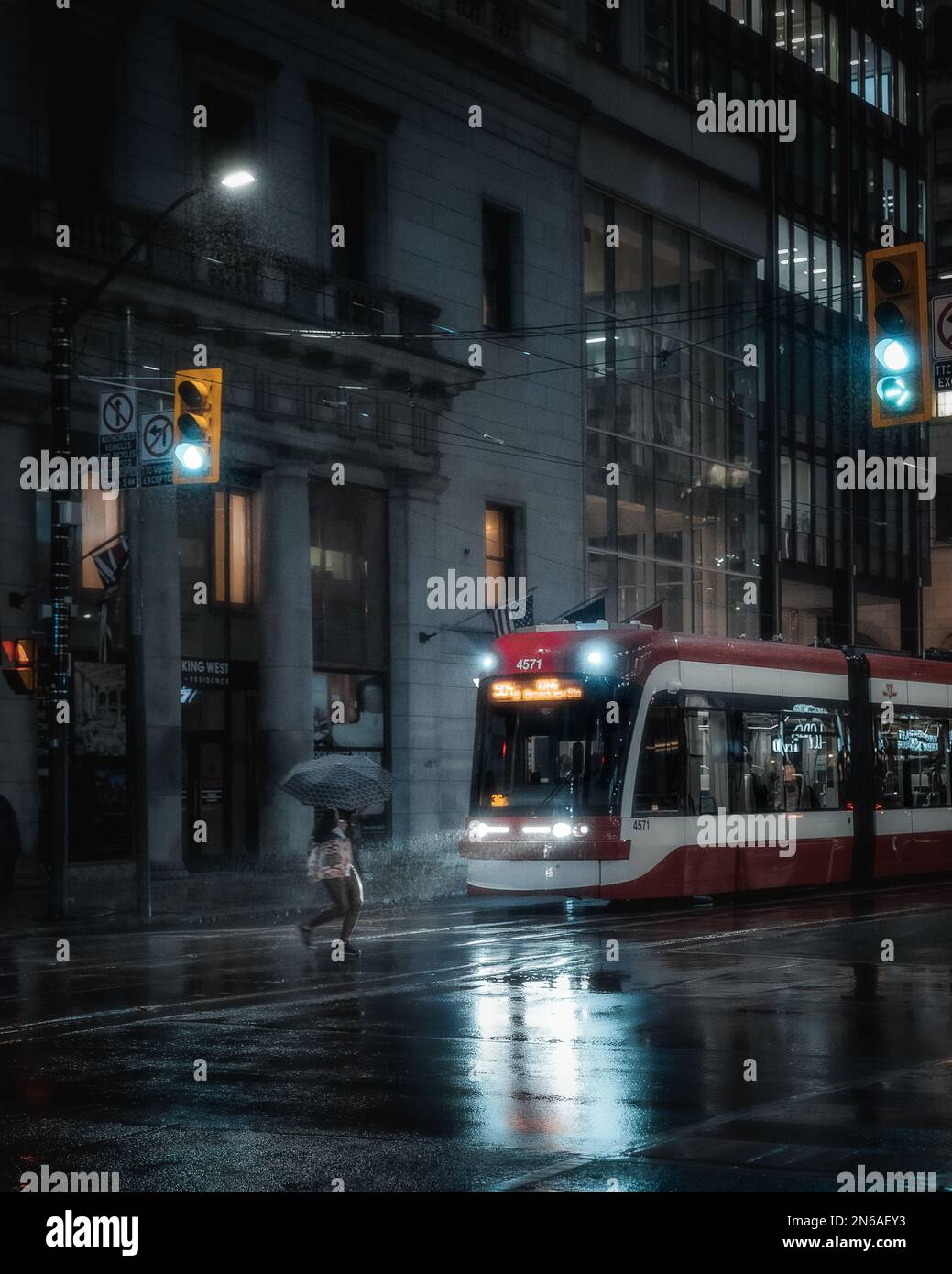 Donne che camminano dall'altra parte della strada sotto la pioggia con un ombrello di fronte al tram di Toronto Foto Stock