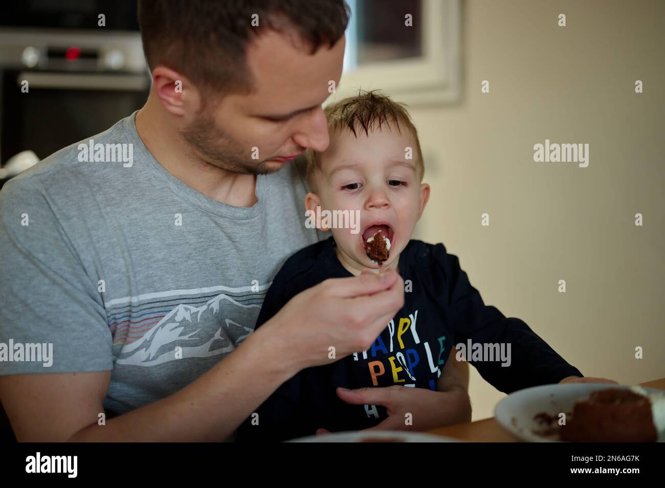 Padre che nutra il bambino piccolo con una torta al cioccolato Foto Stock
