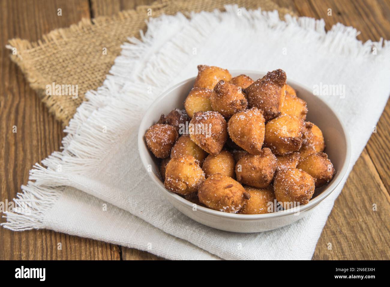 Castagnole fatte in casa, frittelle tipiche italiane di carnevale con zucchero in una ciotola bianca su un rustico tavolo di legno Foto Stock
