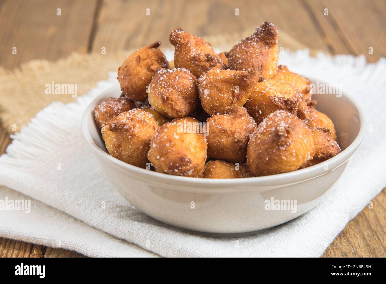 Castagnole fatte in casa, frittelle tipiche italiane di carnevale con zucchero in una ciotola bianca su un rustico tavolo di legno Foto Stock