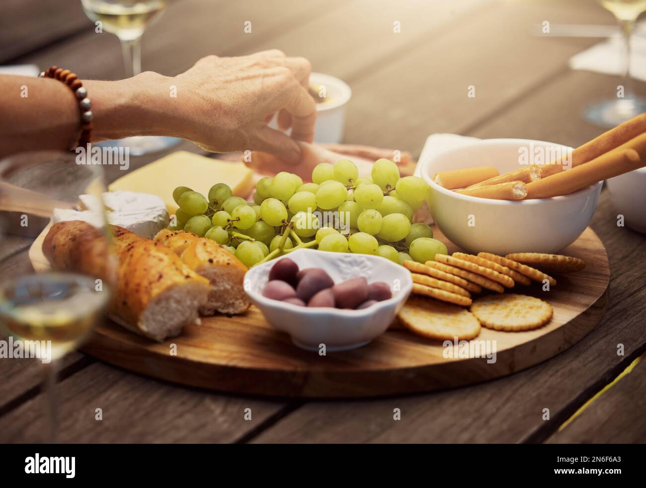 Donna sconosciuta che prende da una varietà di spuntini su una tavola di legno di tapas all'esterno. Formaggi, pane, uva fresca e salumi preparati per il pranzo Foto Stock