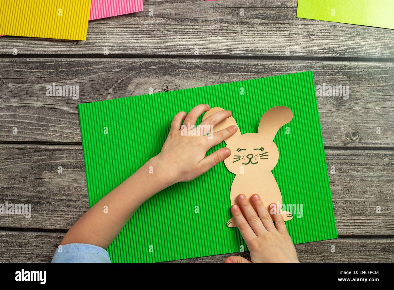 Un bambino fa una cartolina con un coniglietto di Pasqua con le proprie mani. Applicazione di carta multicolore. Coniglietto di pasqua artigianale Foto Stock