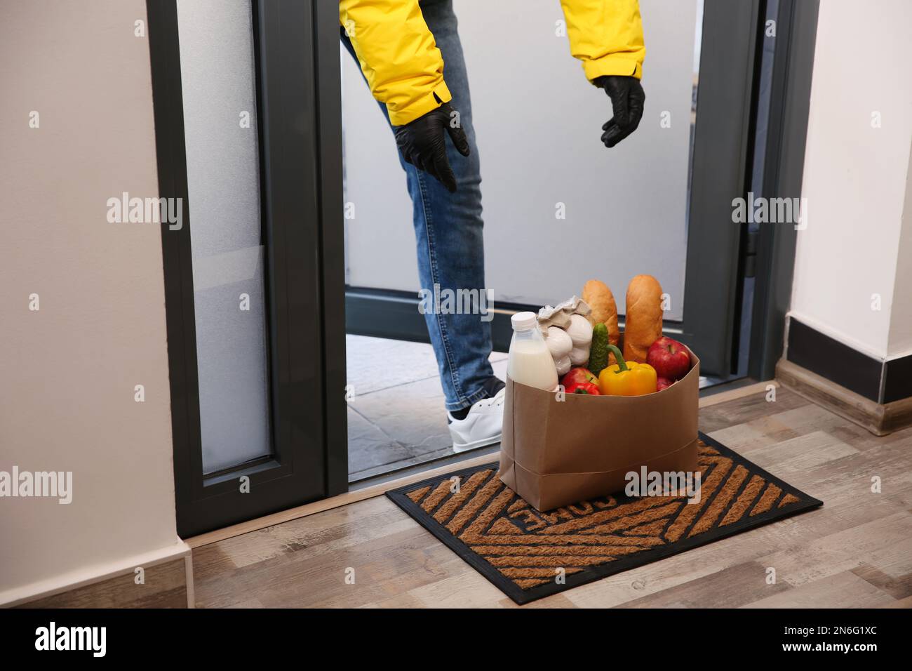 Corriere portare sacchetto di carta con cibo a porta, primo piano. Servizio di consegna durante la quarantena dovuta all'epidemia di Covid-19 Foto Stock