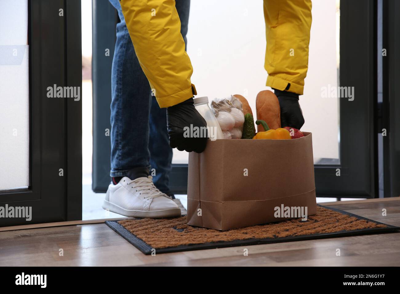 Corriere portare sacchetto di carta con cibo a porta, primo piano. Servizio di consegna durante la quarantena dovuta all'epidemia di Covid-19 Foto Stock