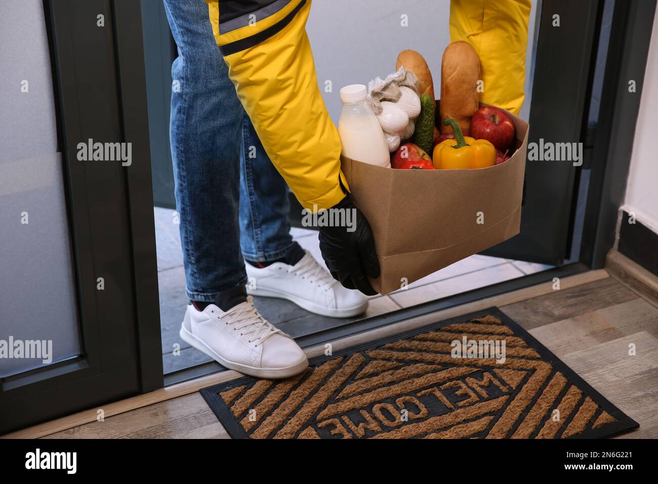 Corriere portare sacchetto di carta con cibo a porta, primo piano. Servizio di consegna durante la quarantena dovuta all'epidemia di Covid-19 Foto Stock