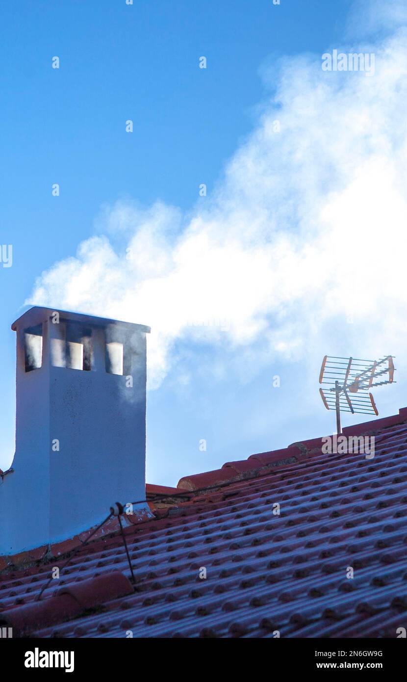 Camino fumoso su un tetto coperto di gelo invernale. sfondo cielo blu Foto Stock